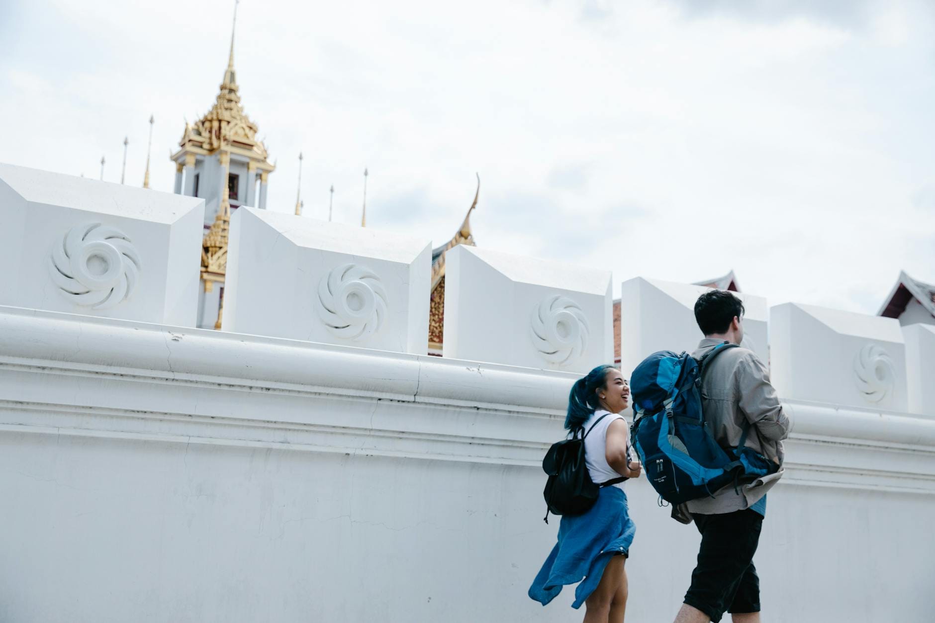 Turyści idący wzdłuż białego muru w Bangkoku z widoczną złotą wieżą świątyni
