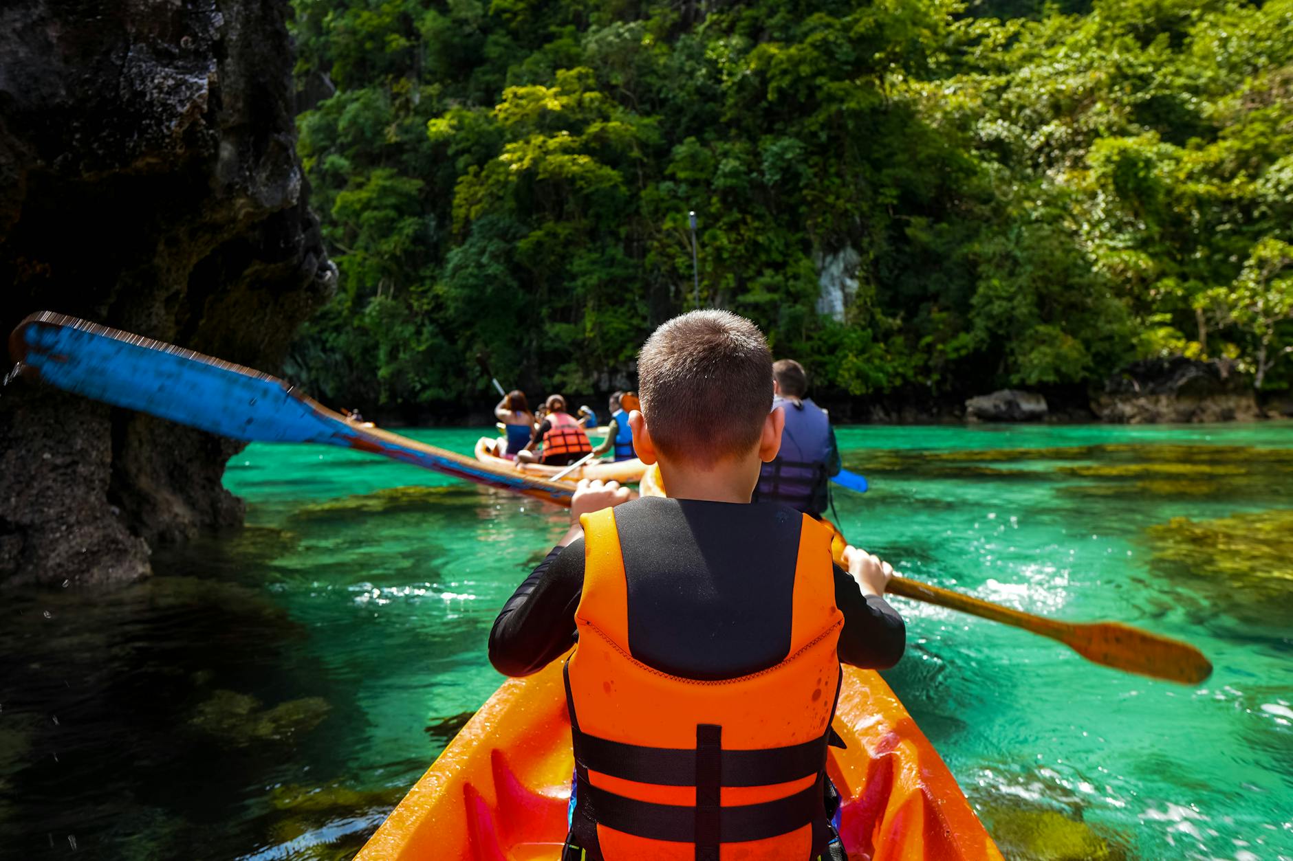 Dzieci płynące kajakami po turkusowej wodzie w otoczeniu zielonego lasu Dzieci płynące kajakami po turkusowej wodzie w otoczeniu zielonego lasu